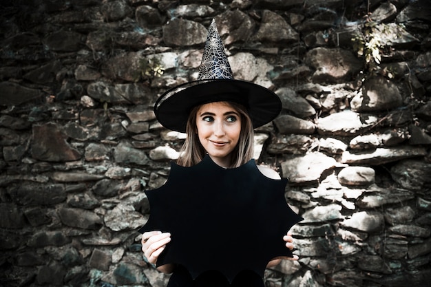 Young woman in witch hat holding Halloween decoration and looking away