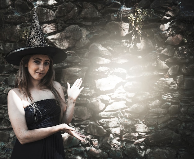 Free Photo young woman in witch hat standing near light spot on wall