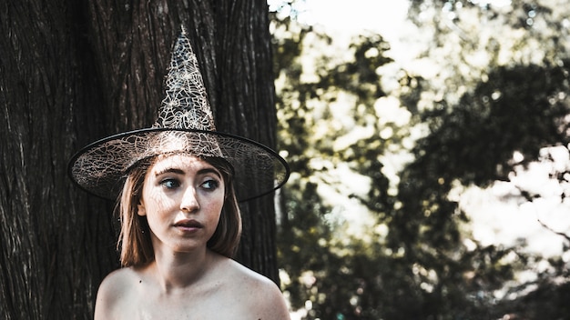 Free photo young woman in witch hat standing near tree