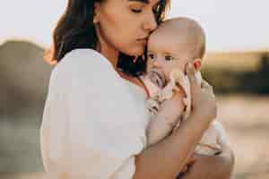 Free photo young woman with baby daughter in carrier on the sunset