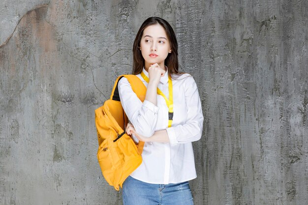 Young woman with backpack standing over gray wall. High quality photo