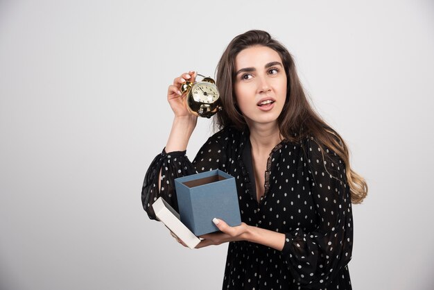 Young woman with blue box holding an alarm clock 