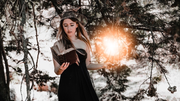 Young woman with book and candle standing in forest