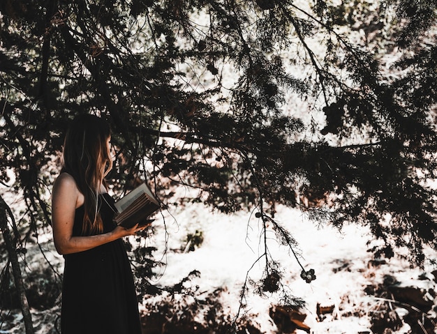 Young woman with book standing in forest