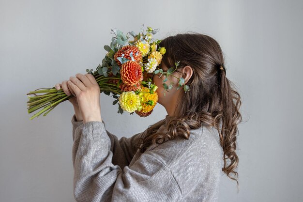 Young woman with a bouquet of fresh chrysanthemums on a gray background