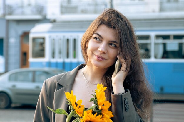 A young woman with a bouquet of sunflowers is talking on the phone at sunset