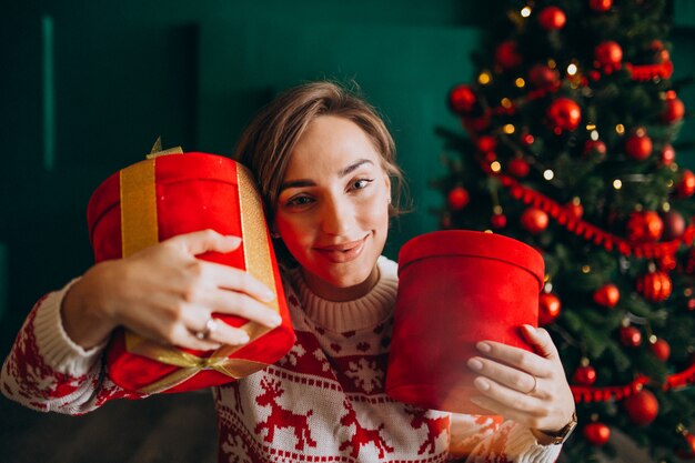 Young woman with Christmas tree holding red boxes