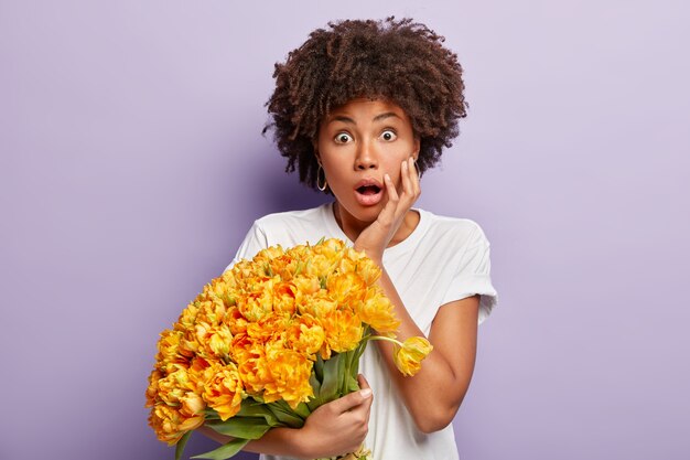 Young woman with curly hair holding bouquet of yellow flowers