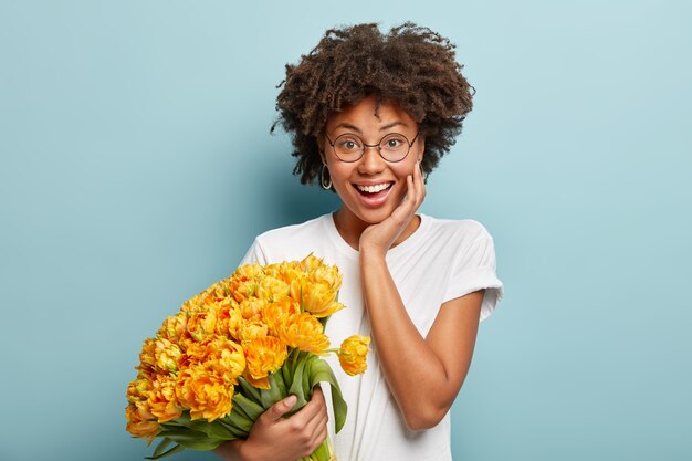 Young woman with curly hair holding bouquet of yellow flowers