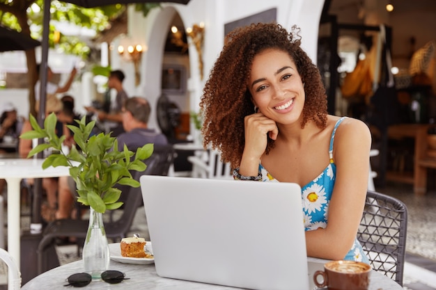 Young woman with curly hair sitting in cafe with laptop