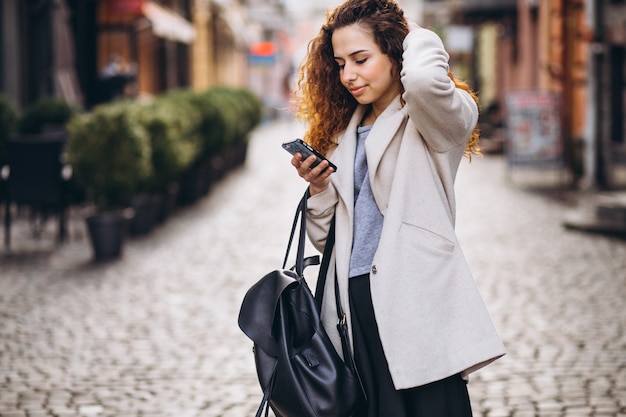 Young woman with curly hair using phone at the street