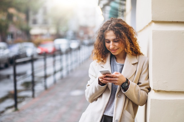 Young woman with curly hair using phone at the street