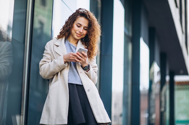 Young woman with curly hair using phone at the street