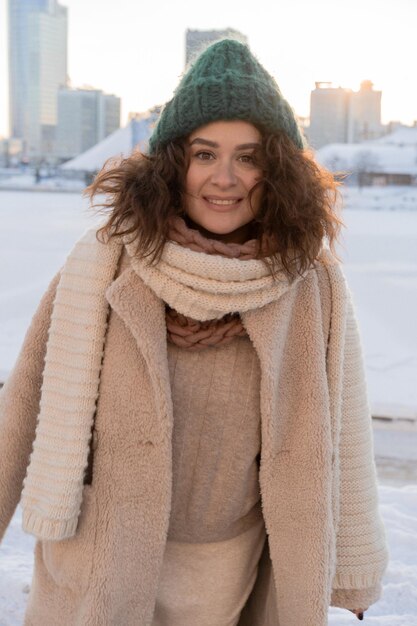 Young woman with dark curly hair in a winter hat, warmly dressed, winter frost, sunny day outside.