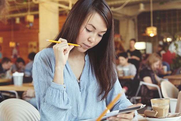 Young woman with dark hair using tablet in cafe