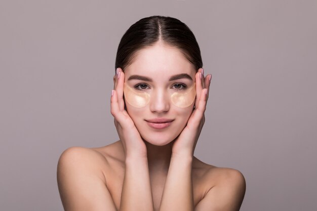 Young woman with an eye patches touching temples isolated on gray wall. Cosmetics, skin stress concept