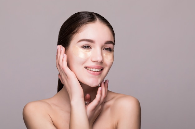 Young woman with an eye patches touching temples isolated on gray wall. Cosmetics, skin stress concept