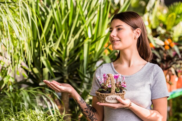 Young woman with flowers in basket showing at green plants