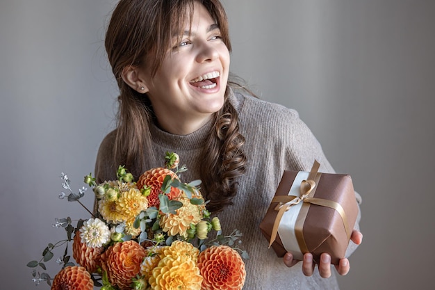 Free photo young woman with a gift box and a bouquet of flowers in her hands