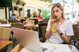 Free photo young woman with glasses on her head smiling joyfully, resting at cafe and browsing internet using laptop computer