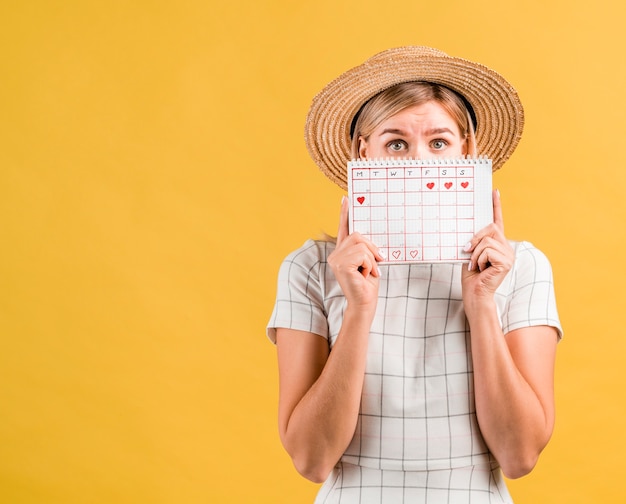 Young woman with hat covering her face with menstruation calendar