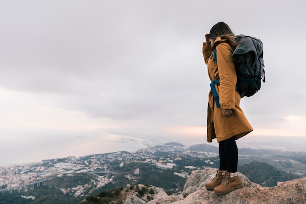 Free photo young woman with her backpack standing on the top of mountain looking at idyllic view