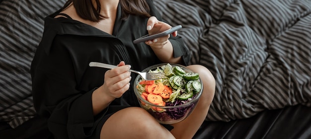 Free photo young woman with a large bowl of fresh salad with vegetables in bed.