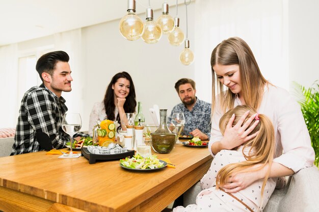 Young woman with little daughter and friends sitting at table