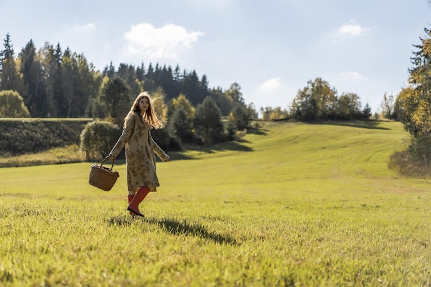 Young woman with long red hair in a linen dress gathering mushrooms in the forest in the bast basket