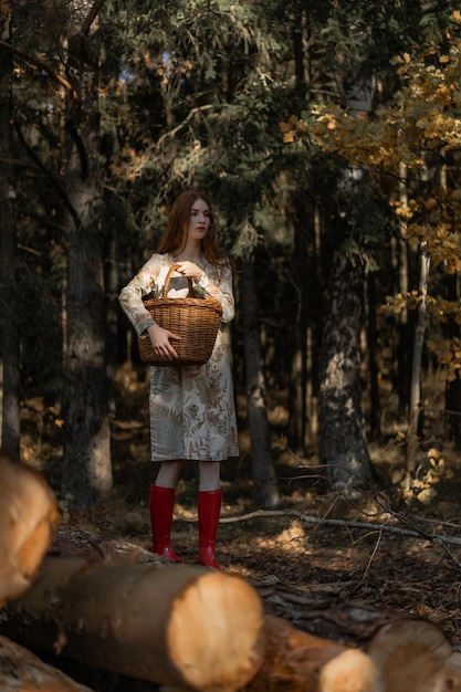 Young woman with long red hair in a linen dress gathering mushrooms in the forest 