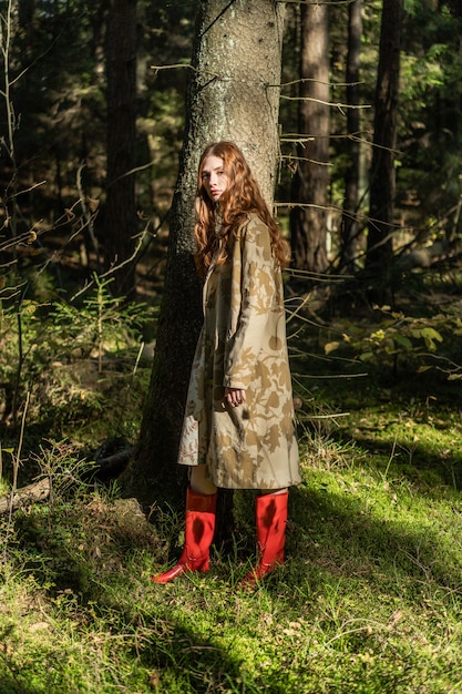 Young woman with long red hair in a linen dress gathering mushrooms in the forest 