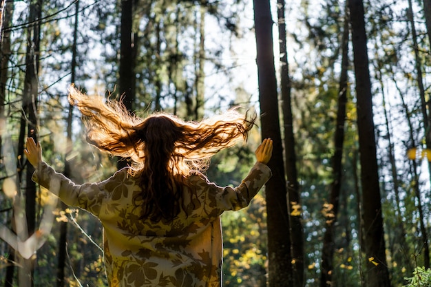 Young woman with long red hair in a linen dress gathering mushrooms in the forest 