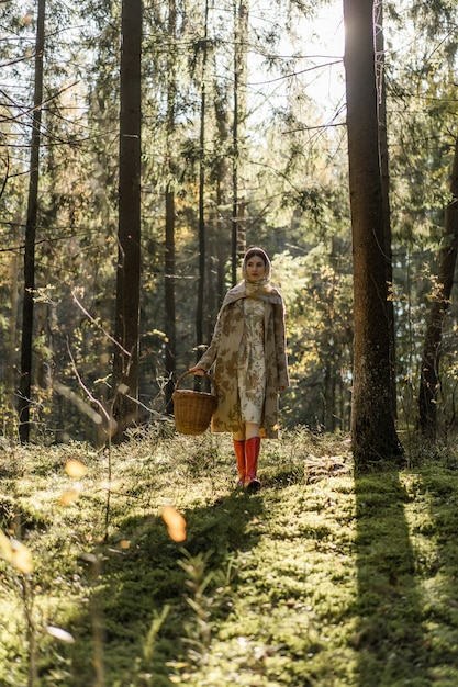 Free photo young woman with long red hair in a linen dress gathering mushrooms in the forest