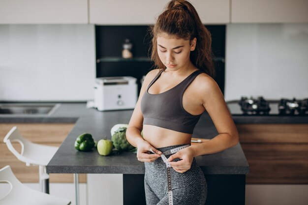 Young woman with measuting tape on weist at the kitchen