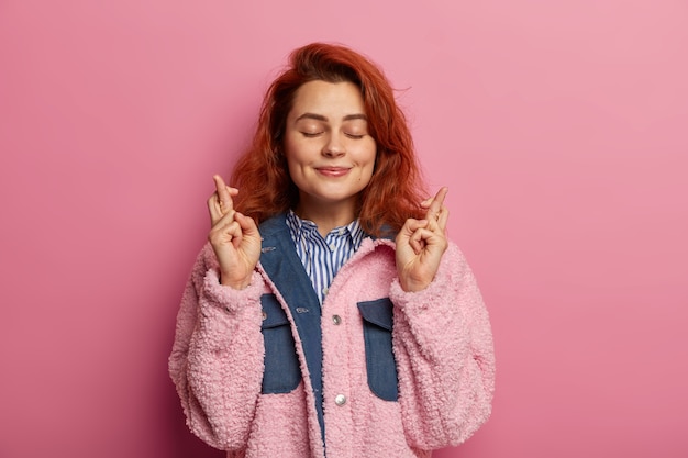 Free Photo young woman with natural wavy ginger hair supports friends, wishes good luck, crosses fingers and awaits for nice result