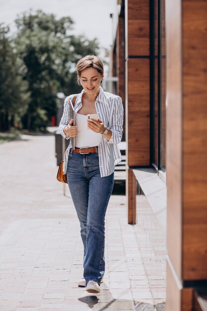 Young woman with phone and computer walking outside the street