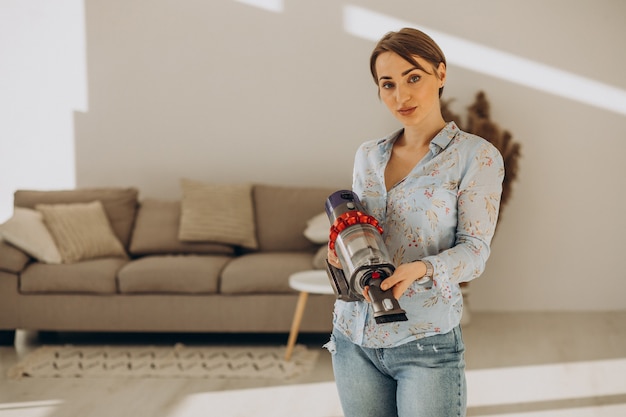 Young woman with rechargeable vacuum cleaner cleaning at home