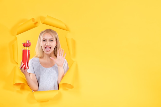 Free photo young woman with red bottle on yellow surface