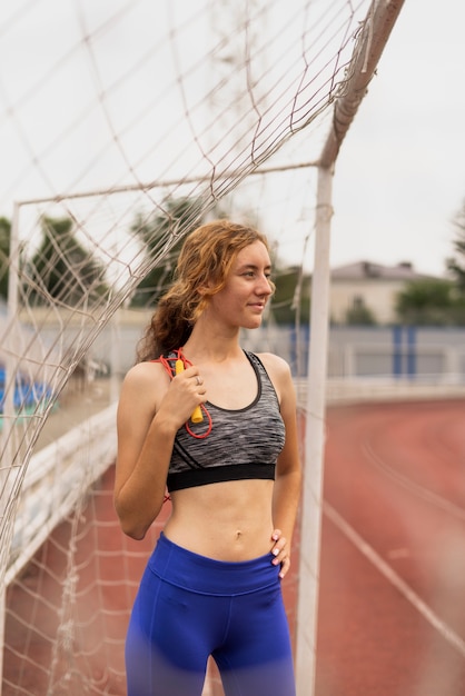 Young woman with rope sitting at footbal gate