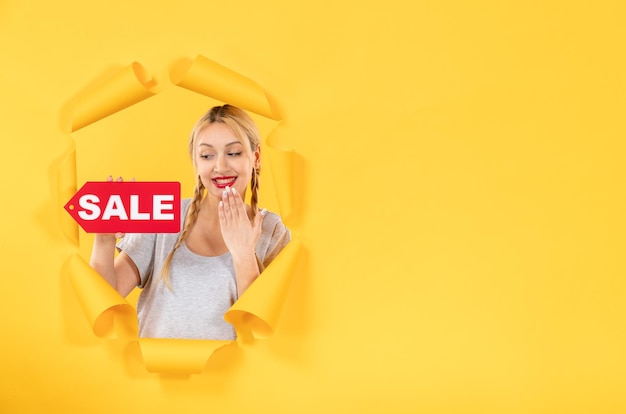 Young woman with sale inscription sign on torn yellow paper background facial indoor shopping