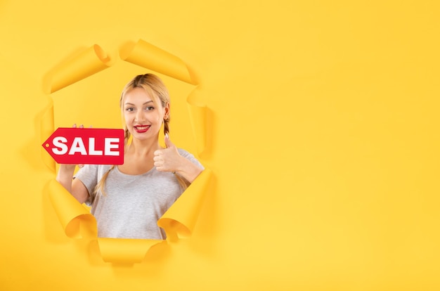 Free photo young woman with sale inscription sign on torn yellow paper background indoor shopping