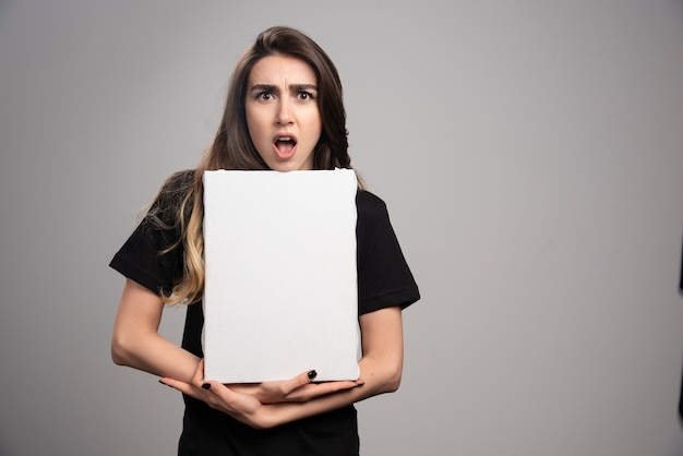 Free Photo young woman with shocked expression holding canvas. 