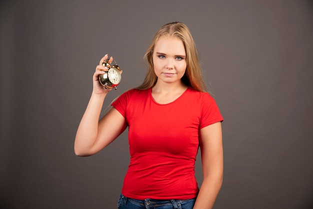 Young woman with small clock standing on black wall.