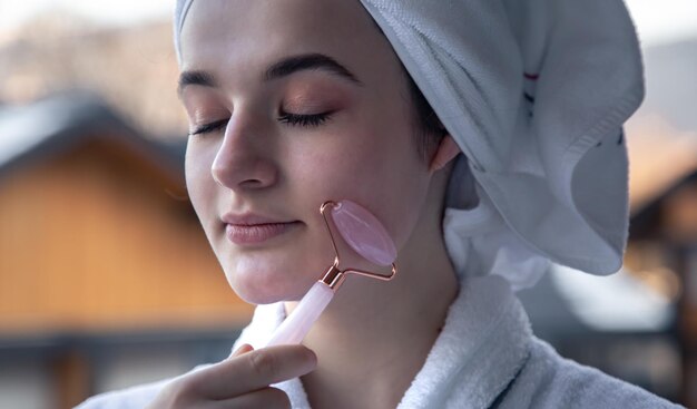 A young woman with a towel on her head is doing a massage with a facial roller