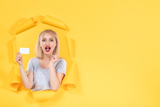 Young woman with white credit card on yellow surface