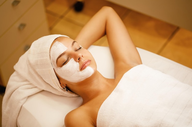 Young woman with white facial mask relaxing with eyes closed at beauty spa