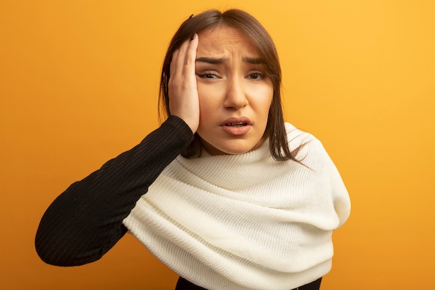 Young woman with white scarf confused with hand on her face 