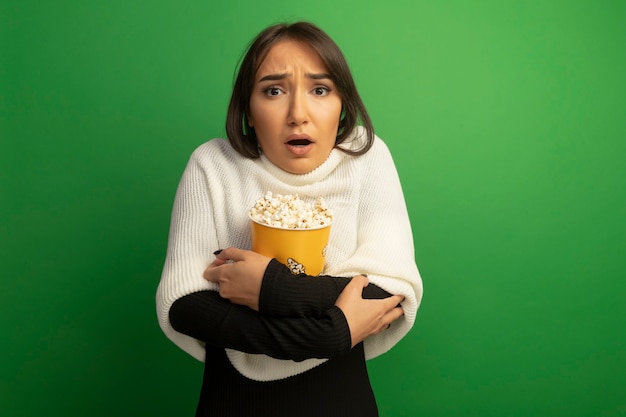 Free Photo young woman with white scarf holding bucket with popcorn worried and confused 