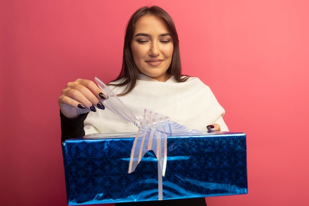 Free photo young woman with white scarf holding gift box trying to pen it smiling with happy face