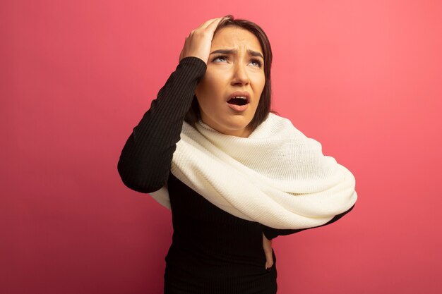 Young woman with white scarf looking confused with hand on head 